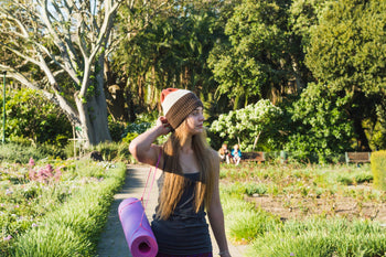 A woman heading to an outdoor yoga session, taking skin protection measures under the sun.